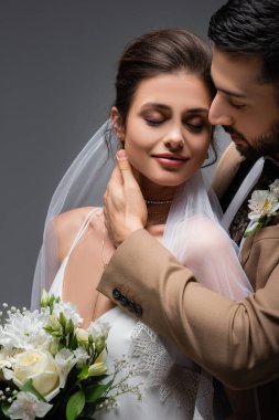 Mutlu, zarif bir kadın, gözleri kapalı, gri renkte izole edilmiş Müslüman damadın yanında duruyor.