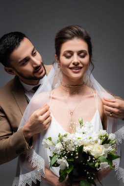 Arap nişanlısı, gri renkte bir buket tutan gelin peçesine dokunuyor.