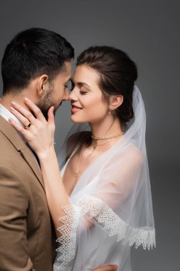 Duvak takmış neşeli bir kadın, gri üzerine izole edilmiş Müslüman damadın yüzüne dokunuyor.