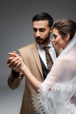 Müslüman adam gri arka planda mutlu gelinin elini tutuyor.