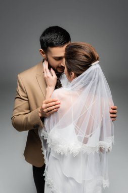 Gri renkte izole edilmiş Müslüman damadın yüzüne dokunan gelinlik giymiş kadının arkadan görünüşü
