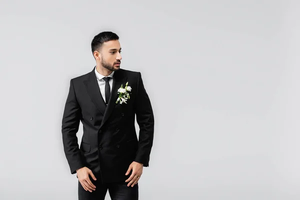 Muslim groom in suit and boutonniere looking away isolated on grey