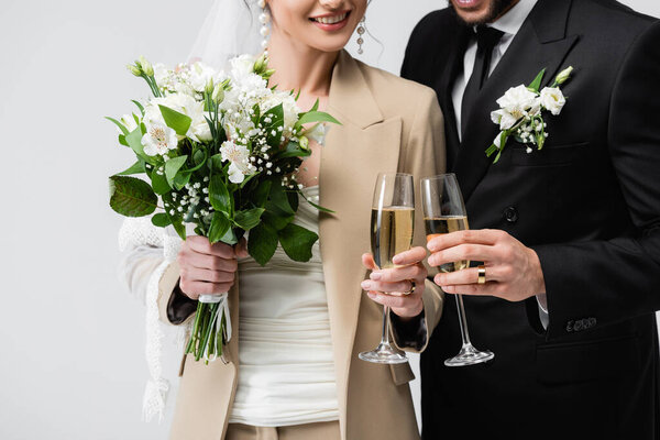 Cropped view of smiling newlyweds toasting with champagne isolated on grey 