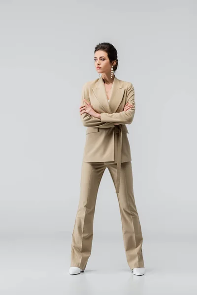 stock image full length view of stylish woman looking away while posing with crossed arms on grey