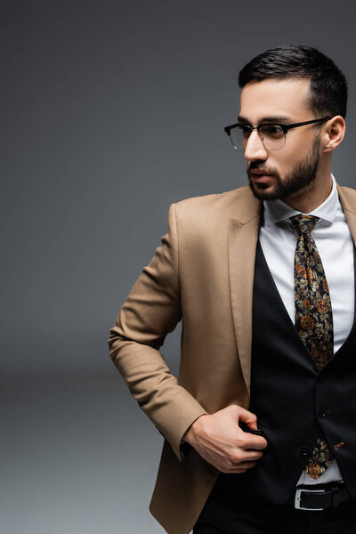 young arabian man in beige blazer and black vest looking away on grey