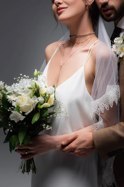 Gri renkte izole edilmiş düğün buketi tutan zarif gelini kucaklayan müslüman manzarası.