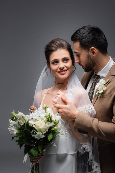 happy woman with wedding bouquet near muslim fiance isolated on grey