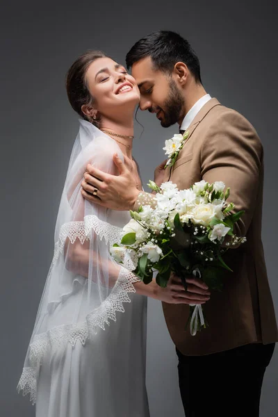 Müslüman damadın yanında düğün buketi tutan neşeli kadın gri yolda izole edilmiş.