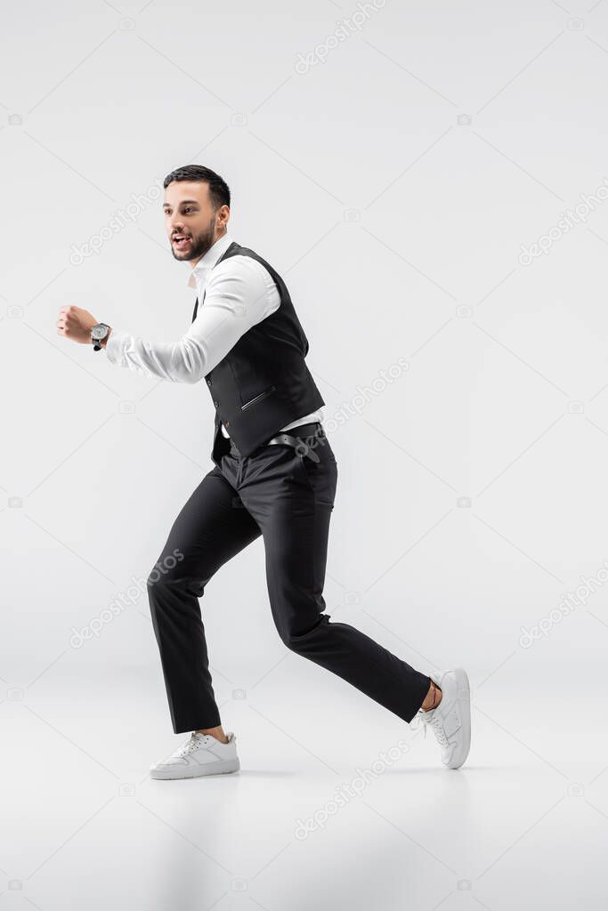 full length view of fashionable arabian man looking away while running on grey