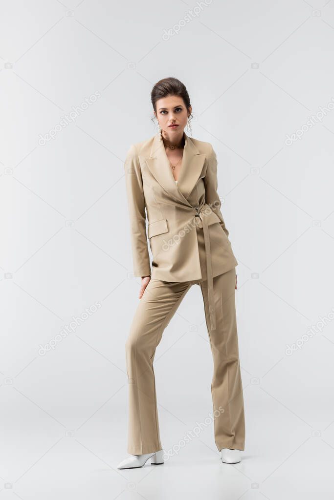 full length view of fashionable brunette woman standing on grey and looking at camera