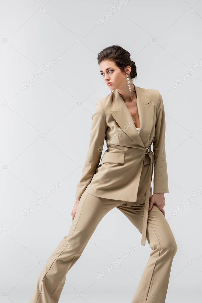 pretty woman in trendy pantsuit looking away while posing isolated on grey