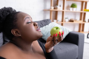 Afrikalı Amerikalı, iri yarı, yeşil elma tutan, gözleri kapalı bir kadın. 