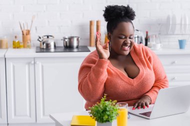 Mutlu Afro-Amerikan artı evde dizüstü bilgisayar kullanarak elini kaldıran bir serbest çalışan.