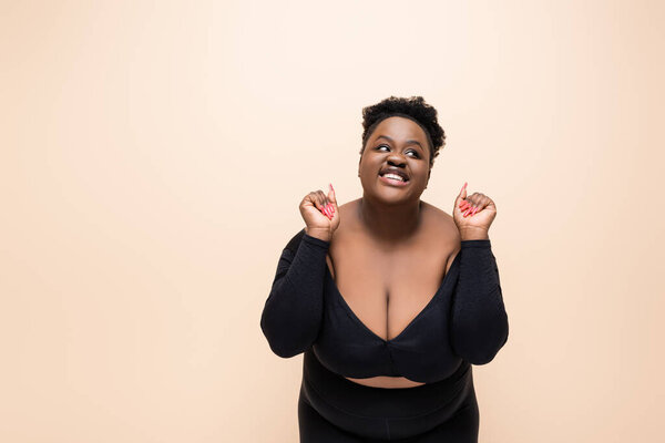 возбужденный африканский американец плюс размер женщина смотрит вдали изолированы на бежевый 