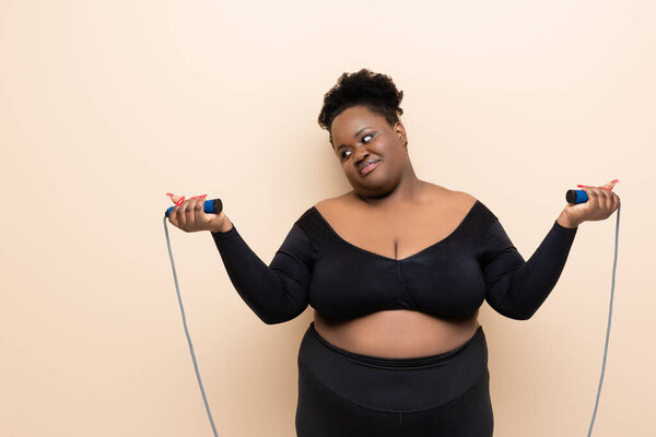 Африканский американец плюс размер женщины в спортивной одежде держа скакалку изолированы на бежевый