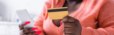 partial view of african american plus size woman holding credit card and smartphone, banner clipart