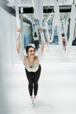 Bulanık arka planda sinek yogası kayışıyla ısınırken mutlu kadın bakışlarını kaçırıyor.