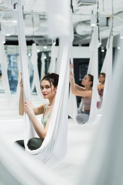 Genç bir kadın, arka planda sineklerle yoga yaparken kameraya bakıyor.