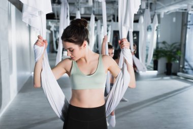 Güzel bir kadın arka planda hava yogası kayışıyla ısınıyor.