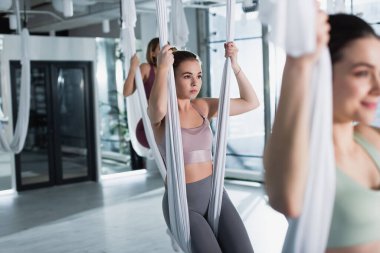 young sportive women practicing aerial yoga in gym, blurred foreground clipart