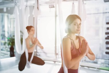 Hava yogası hamağında poz verirken kameraya bakan genç kadın, bulanık arkaplan