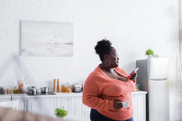 happy african american plus size woman holding on smartphone and cup of coffee
