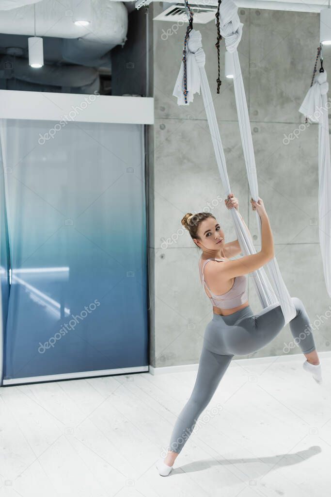 young sportswoman stretching with fly yoga hammock in gym