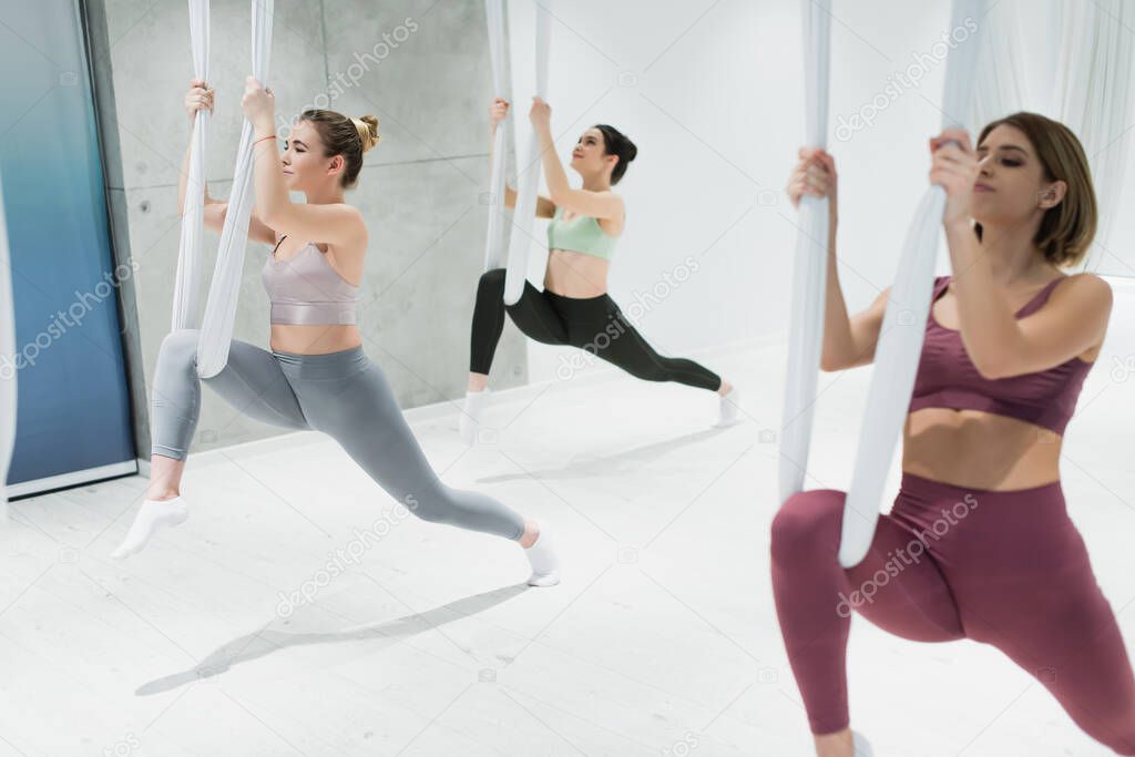 three young sportswomen practicing aerial yoga on blurred foreground