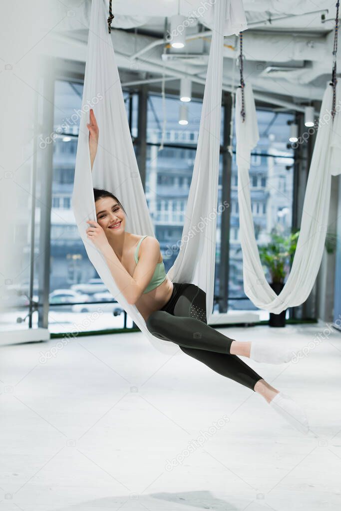 happy woman looking at camera while relaxing in fly yoga hammock
