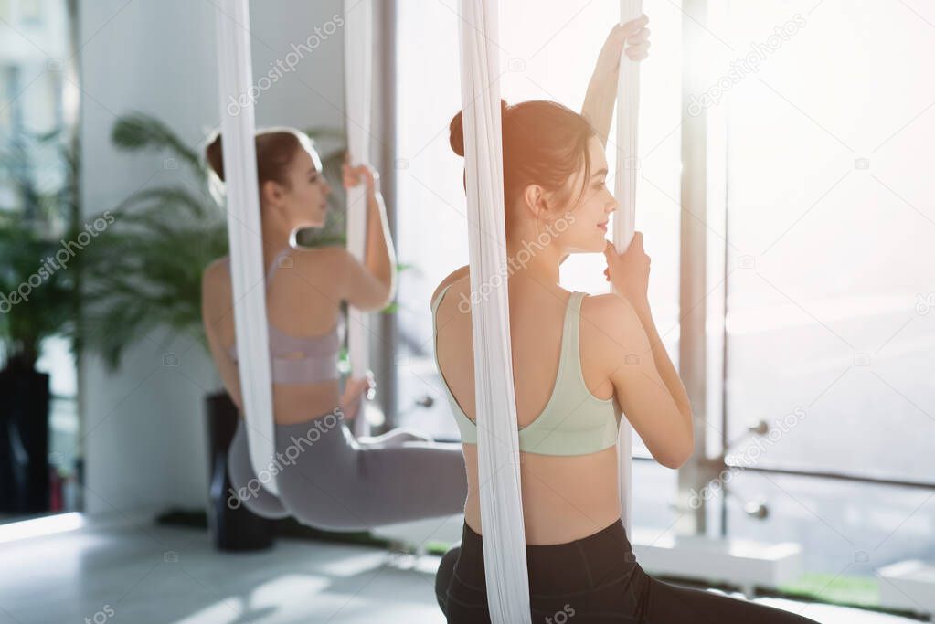 young sportive women meditating in lotus pose while practicing fly yoga, blurred background