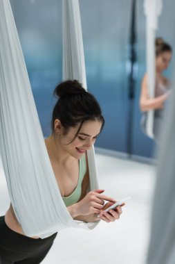 Sinek yogası eğitiminde cep telefonu kullanan neşeli bir kadın. 