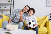 usmívající se muslim muž ukazuje s rukou blízko syna při sledování fotbalového mistrovství doma