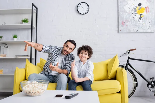 Gülümseyen Arap Adam Evdeki Oğluyla Televizyon Izlerken Parmaklarıyla Işaret Ediyor — Stok fotoğraf