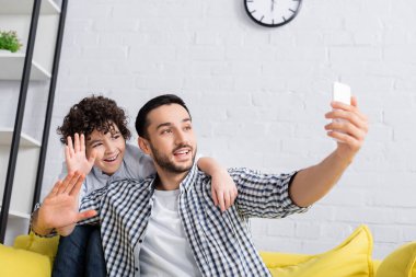 Neşeli Arap baba ve oğlu cep telefonuyla video görüşmesi sırasında el sallıyorlar.