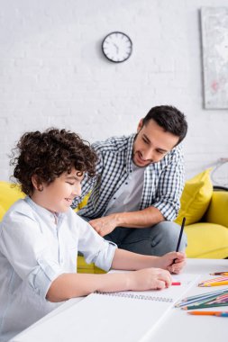 Neşeli Arap çocuk çizim defterinde kurşun kalemle mutlu babasının yanına çiziyor.