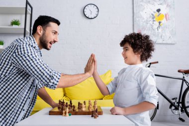 Neşeli Müslüman baba ve oğul güvertede satranç oynarken beşlik çakıyor. 