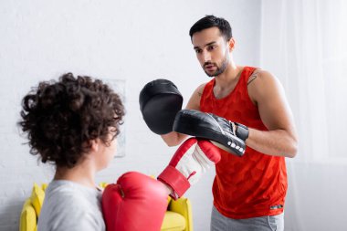 Yumruk eldivenli Arap bir adam oğlu boks eldivenli ön planda bulanık duruyor. 