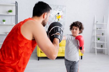 Arabian boy boxing with father on blurred foreground in living room  clipart