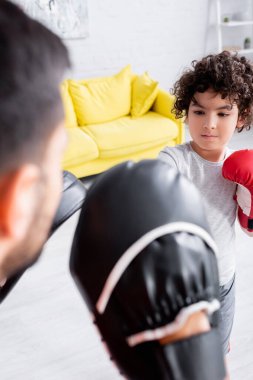 Muslim boy boxing during training with father in punch mitts on blurred foreground  clipart