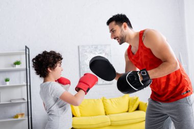 Gülümseyen Arap adam evde oğluyla boks eldiveni giyiyor. 