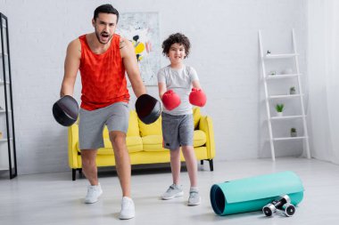 Heyecanlı Müslüman baba yumruklarıyla oğlunun yanında duruyor ve evde spor aletleri var. 