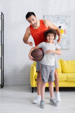 Neşeli Müslüman oğul ve baba evde basketbolu işaret ediyor. 