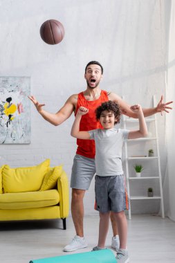 Excited arabian father and son standing near basketball at home  clipart