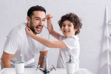Banyoda babasının kaşlarının yanında cımbız tutan neşeli Arap çocuk. 