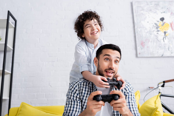 КИЕВ, УКРАИНА - 15 ЯНВАРЯ 2021: весёлый арабский мальчик с взволнованным отцом, играющий в видеоигры дома