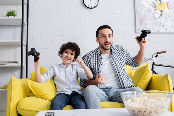 КИЕВ, УКРАИНА - 15 ЯНВАРЯ 2021: счастливые арабский ребенок и отец держа джойстики и показывая жест успеха