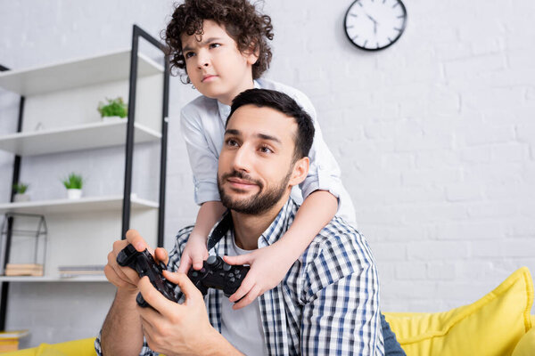 КИЕВ, УКРАИНА - 15 ЯНВАРЯ 2021: сконцентрированный арабский мальчик играет в видеоигры вместе со скептически настроенным отцом