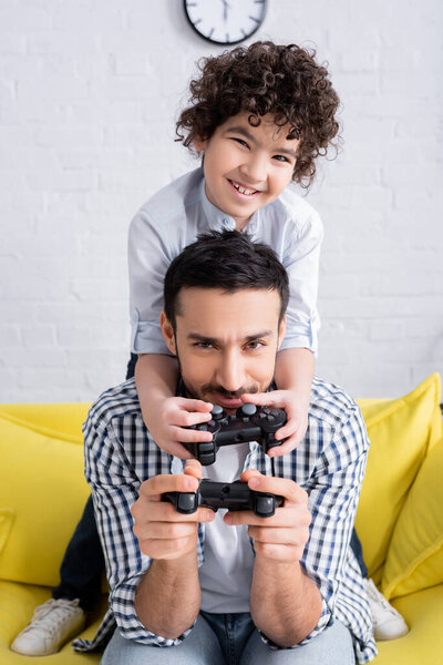 КИЕВ, УКРАИНА - 15 ЯНВАРЯ 2021: весёлый арабский мальчик играет в видеоигры с отцом дома