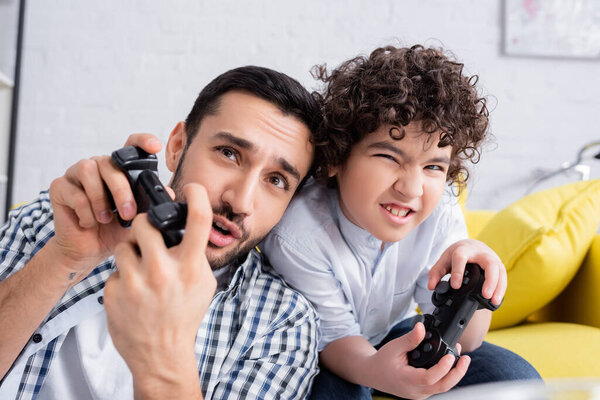 КИЕВ, УКРАИНА - 15 ЯНВАРЯ 2021: взволнованный арабский ребенок и отец играют в видеоигры дома