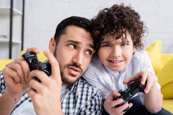 КИЕВ, УКРАИНА - 15 ЯНВАРЯ 2021: скептически настроенный арабский мужчина смотрит на взволнованного сына, играя вместе дома